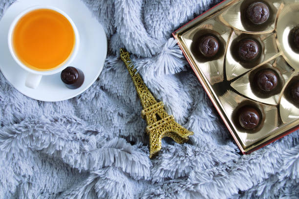 cup of green tea, a box of chocolates and an eiffel tower figurine on a fur blanket. - eiffel tower paris france france tower imagens e fotografias de stock