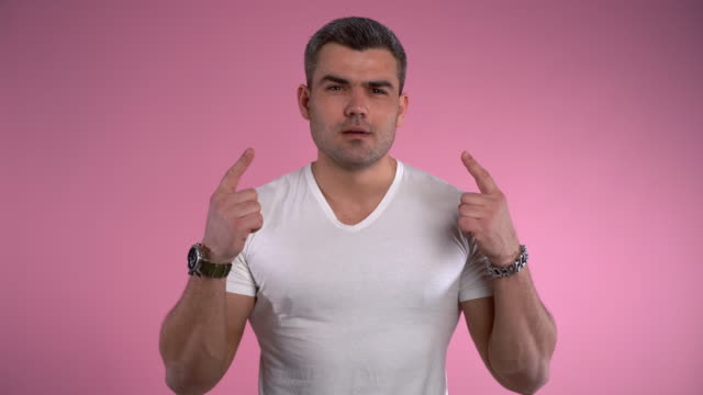 Handsome man gesturing with hands on pink background and pointing firstly to the left and then to the right. Copy space for advertisement, gestures and emotions