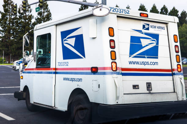 A lineup of United States Postal Service vans parked in a lot.