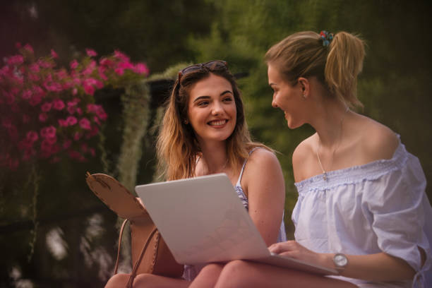 istock Two females flirting while relaxing outdoors and using laptop together 1198926266
