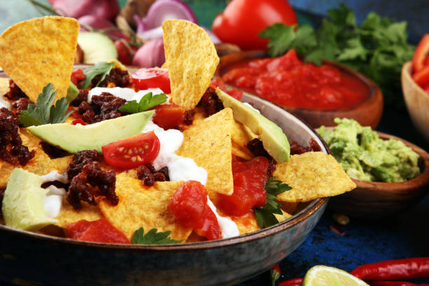 istock mexican nacho chips garnished with ground beef, guacamole, melted cheese, peppers and cilantro leaves in plate 1198928181