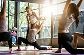 Group of multi ethnics people learning Yoga class in fitness club. Female Caucasian instructor coaching and adjust correct pose to Asian girl student at front while others doing follow them.