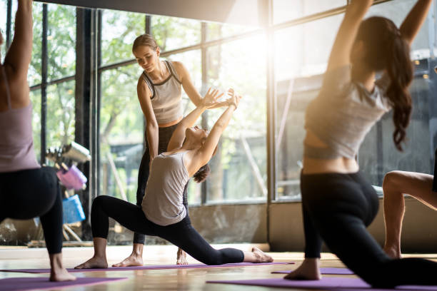 grupa wieloetnicznych ludzi uczących się zajęć jogi w klubie fitness. kobieta kaukaski instruktor coaching i dostosować prawidłowe stanowią do asian student dziewczyna z przodu, podczas gdy inni robią za nimi. - yoga class instructor yoga exercising zdjęcia i obrazy z banku zdjęć