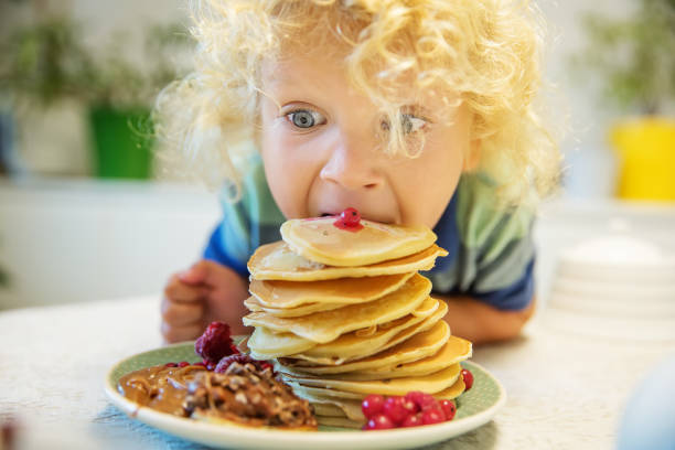istock Little curly boy eating sweet pancakes 1198931471