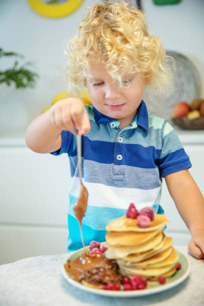 istock Little curly boy eating sweet pancakes 1198931472