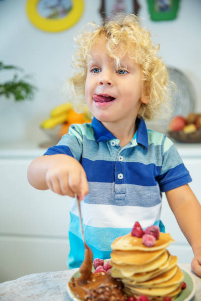 istock Little curly boy eating sweet pancakes 1198931473