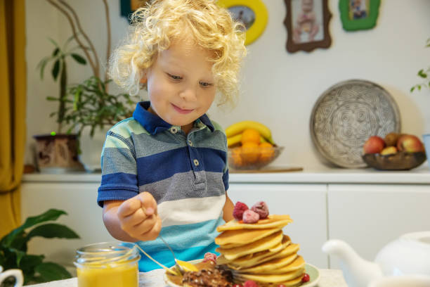 istock Little curly boy eating sweet pancakes 1198931485