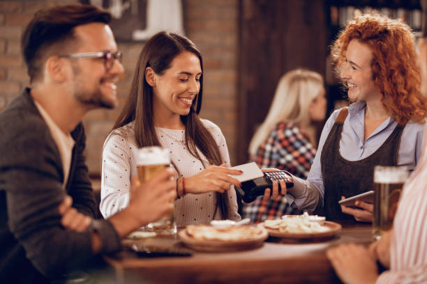 istock Young woman using smart phone while paying a bill in a pub. 1198943525