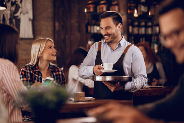 istock Happy waiter communicating with customers while serving them coffee in a pub. 1198944429
