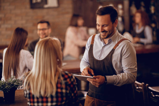 istock Happy waiter talking to a woman while writing her order on touchpad in a bar. 1198946111