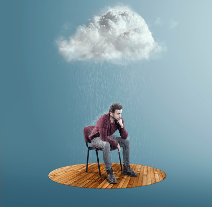 Thoughtful man sits on chair with a cloud above and raining.