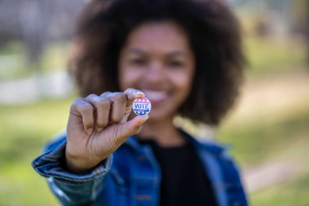 Voting A young African American woman holding a voting badge. voter registration stock pictures, royalty-free photos & images