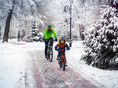 Man and his son ride bicycles along a bicycle path in a winter park. Back view. Father and son spend an active weekend in the park