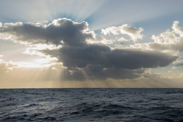 istock Sunbeams or light rays in a cloudy sky over the ocean. 1198976500