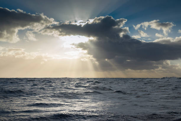 istock Sunbeams or light rays in a cloudy sky over the ocean. 1198976504
