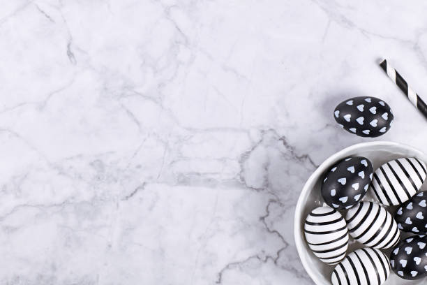 Easter flat lay with top view of bowl with modern black and white painted easter eggs in lower corner and blank copy space on marble background