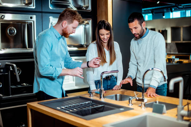 Young husband and wife buying equipment for their first kitchen in a specialized shop with a salesman providing them assistance Young couple shopping together in a kitchen equipment store with a salesman helping them. showroom stock pictures, royalty-free photos & images