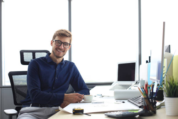 istock Handsome male architect looking at camera and smiling while sitting in the office. 1198990687