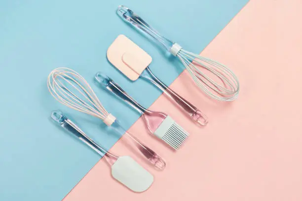 Blue and pink silicone kitchen utensils ob pink and blue background, top view