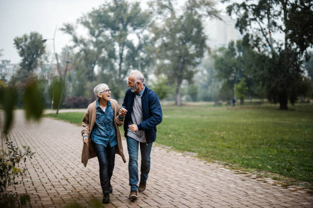 手をつないで公園を走りながら楽しむ陽気なシニアカップル。 - senior adult fun autumn senior couple ストックフォトと画像