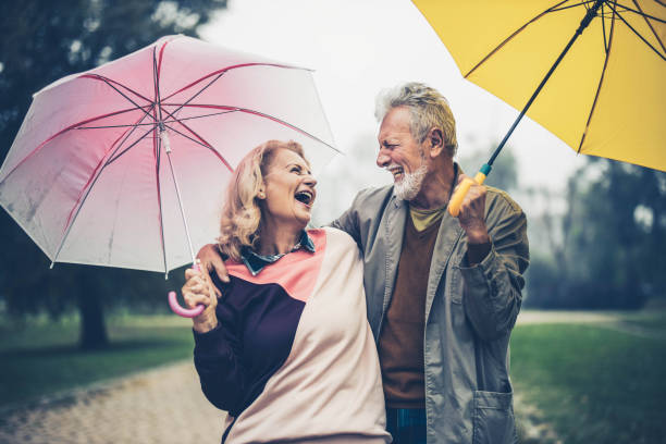 couples aînés joyeux avec des parapluies parlant dans la nature. - umbrella senior adult couple autumn photos et images de collection