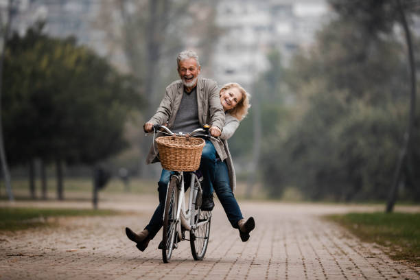 verspieltes seniorenpaar, das sich am herbsttag auf dem fahrrad amüst. - women winter autumn nature stock-fotos und bilder