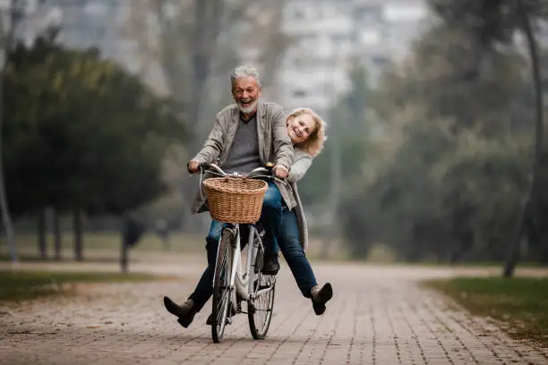 Photo of Playful senior couple having fun on a bike in autumn day.