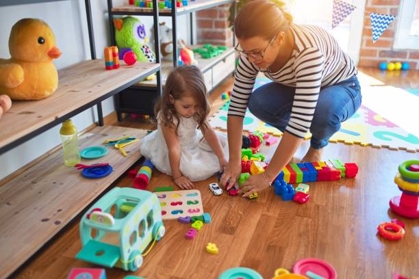 schöne lehrerin frau und kleinkind spielen um viele spielzeuge im kindergarten - child playroom parent indoors stock-fotos und bilder