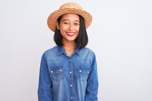 Young beautiful chinese woman wearing denim shirt and hat over isolated white background with a happy and cool smile on face. Lucky person.