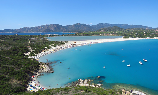 Panorama coastal view over sand beach, tranquil bay, distant mountains and blue water of the Mediterranean Sea, Porto Giunco, Sardinia, Italy, Europe