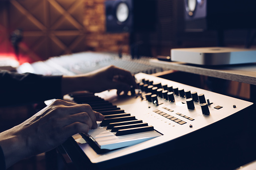 male musician hands playing keyboard synthesizer in recording studio