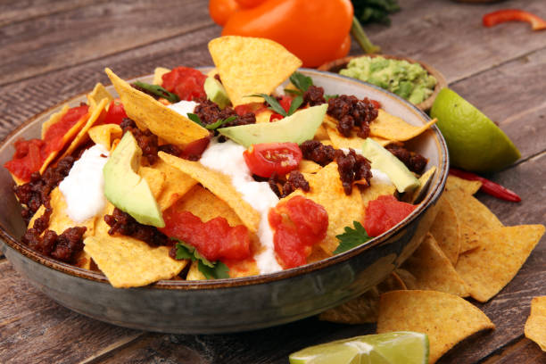 istock mexican nacho chips garnished with ground beef, guacamole, melted cheese, peppers and cilantro leaves in plate 1199004407