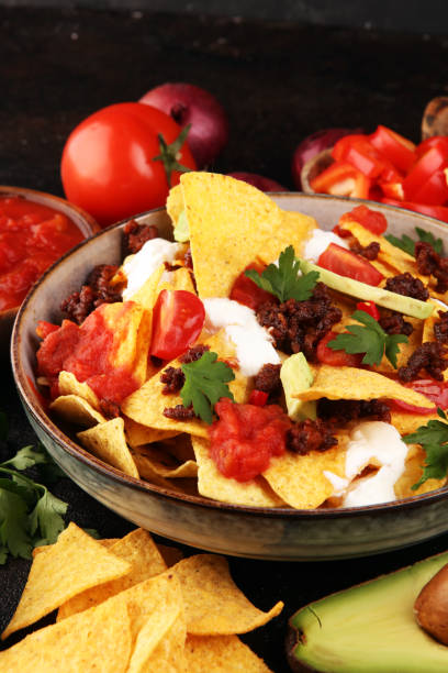 istock mexican nacho chips garnished with ground beef, guacamole, melted cheese, peppers and cilantro leaves in plate 1199005528