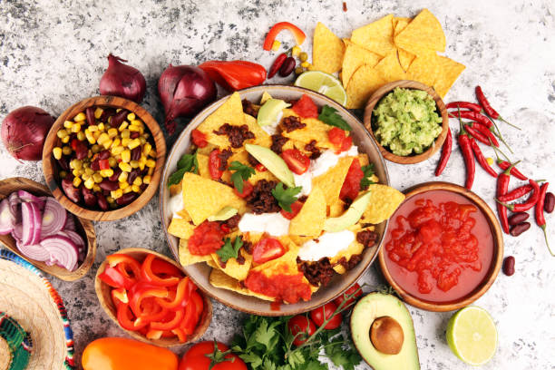 istock mexican nacho chips garnished with ground beef, guacamole, melted cheese, peppers and cilantro leaves in plate 1199005615