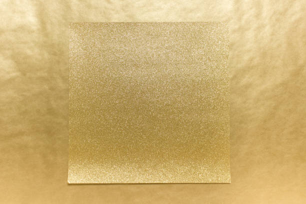 Square sheet of golden glitter paper on golden craft paper background.