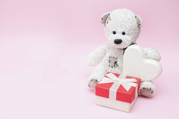 istock Teddy Bear holding a heart and gift on pink background, copy space 1199008527