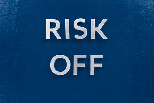 the words risk off laid with silver metal letters on classic blue surface for stock market strategy background.