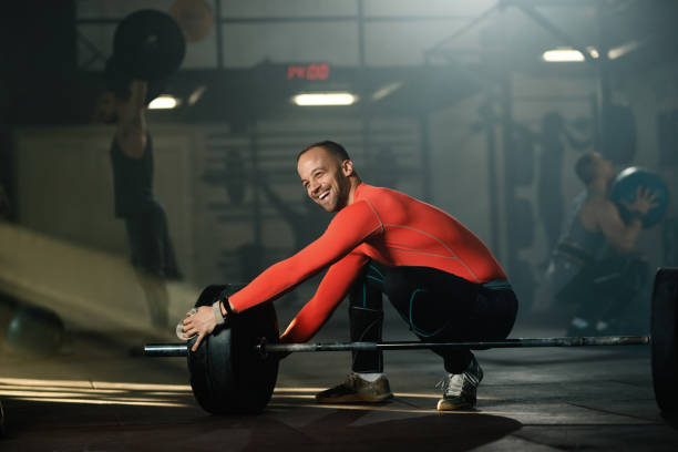sportivo felice che prepara il bilanciere per l'allenamento con i pesi in palestra. - crouching barbell weightlifting weight training foto e immagini stock