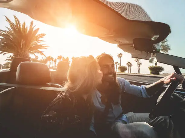 Happy people having fun in convertible car in summer vacation at sunset - Young couple enjoyng  holiday on cabrio auto outdoor - Travel, youth lifestyle and wanderlust concept - Soft focus on man face