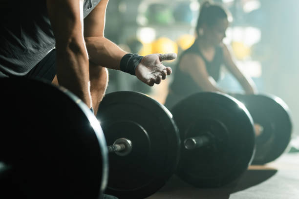 Unrecognizable bodybuilder using sports chalk while preparing for weightlifting in a gym. Unrecognizable muscular build man preparing his hands with talcum powder on weight training in health club. Focus is on hand. crossfit chalk weightlifting weight training stock pictures, royalty-free photos & images