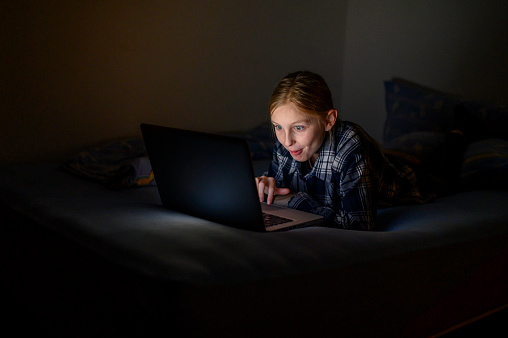 Teenage girl using laptop at night in the bed.