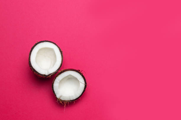 Ripe half coconut on pink colored background, minimal flat lay style top view.