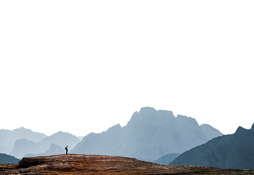 Distant tiny person in a background of mountains range isolated on white background, lonely hiker looking at view in vast environment