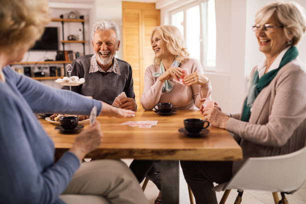 istock Cheerful senior friends playing cards while gathering at home. 1199017489