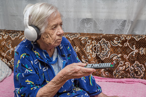 A very old woman with headphones is watching TV