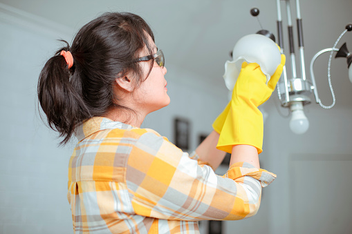 asian woman replacing lamp at living room