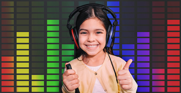 Positive mixed race girl wearing headphones getting hearing test, audiometry, sound equalizer on the background. Child hearing exam