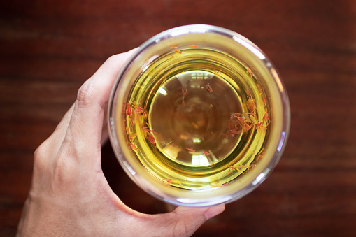 Women hand holding a cup of Safflower herbal tea with wooden table background; tea for reducing blood pressure and cholesterol. Good health concept, Top view.