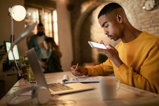 istock Young black entrepreneur writing reports while talking on the phone in the office. 1199028309