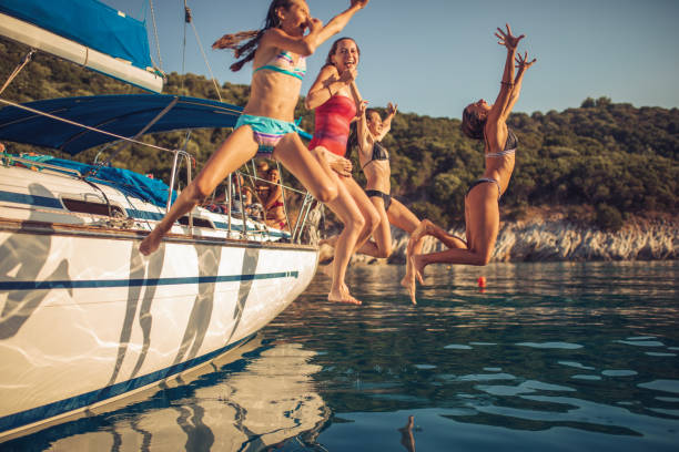 People on vacation have a fun while jumping into the sea from sailboat deck. They are very playful and happy.